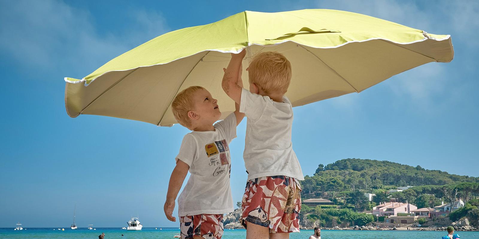 Malé děti stavějící slunečník na pláži